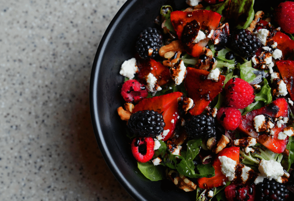 a medley of berries with spring mix, feta cheese, is displayed over a black plate and balsamic drizzle